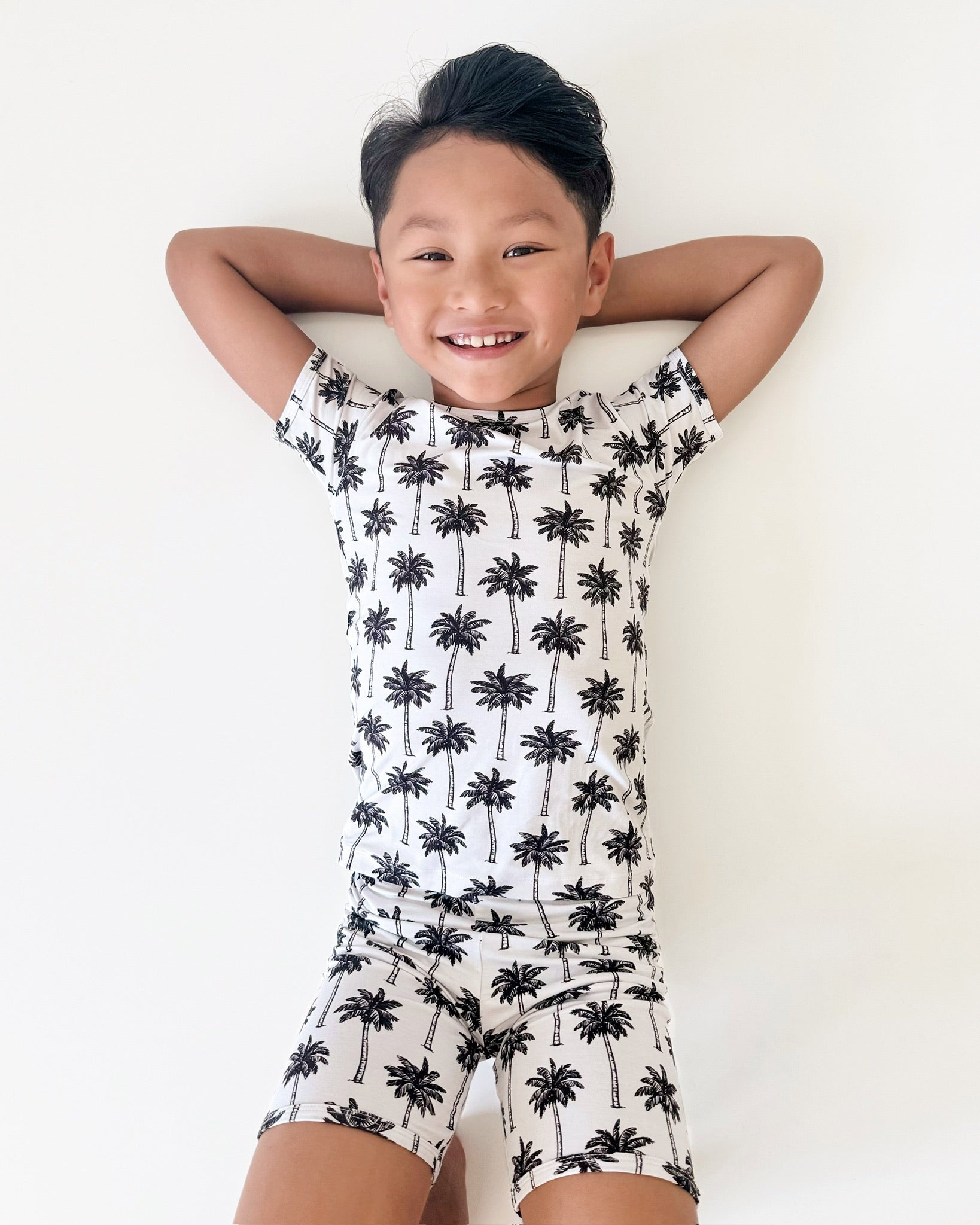Smiling child wearing a palm print bamboo shorts set, featuring a tee and shorts, perfect for summer adventures.