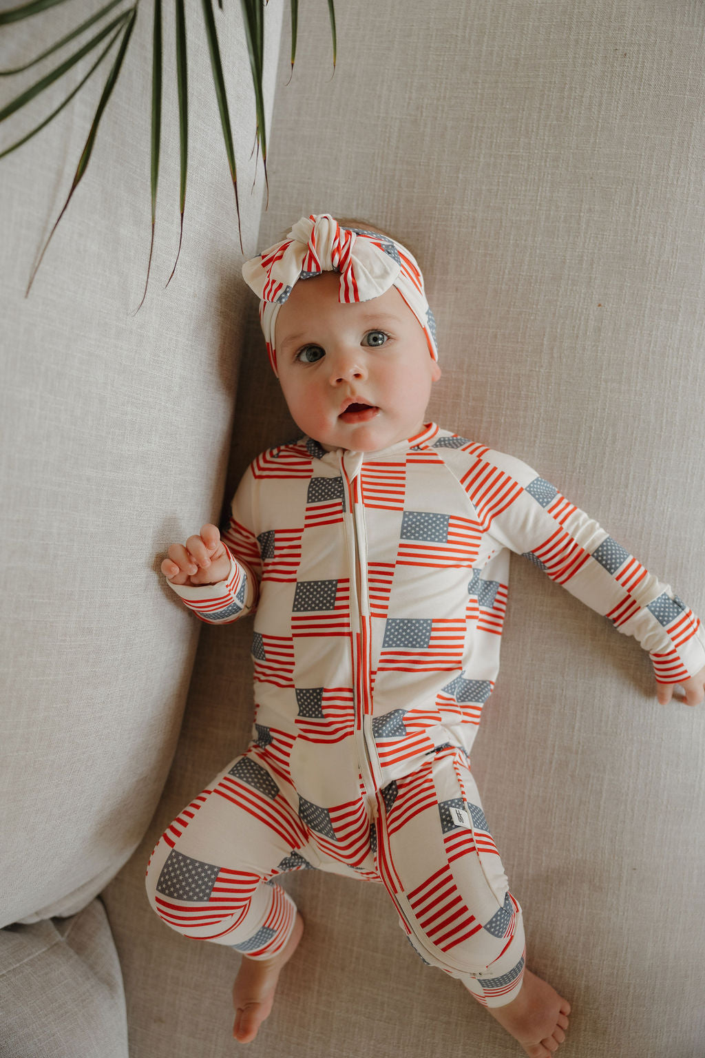 Infant wearing Americana bamboo zip pajamas with stars and stripes design, featuring cozy double zipper and matching headband.