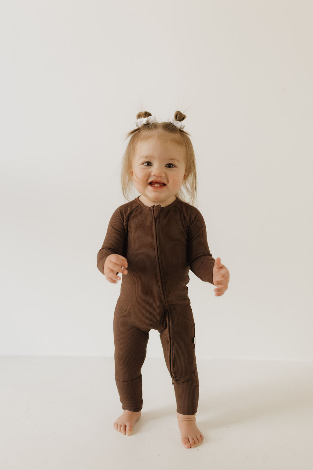 Child wearing Coffee Bean bamboo zip pajamas, smiling and ready for cuddles in a cozy brown outfit.