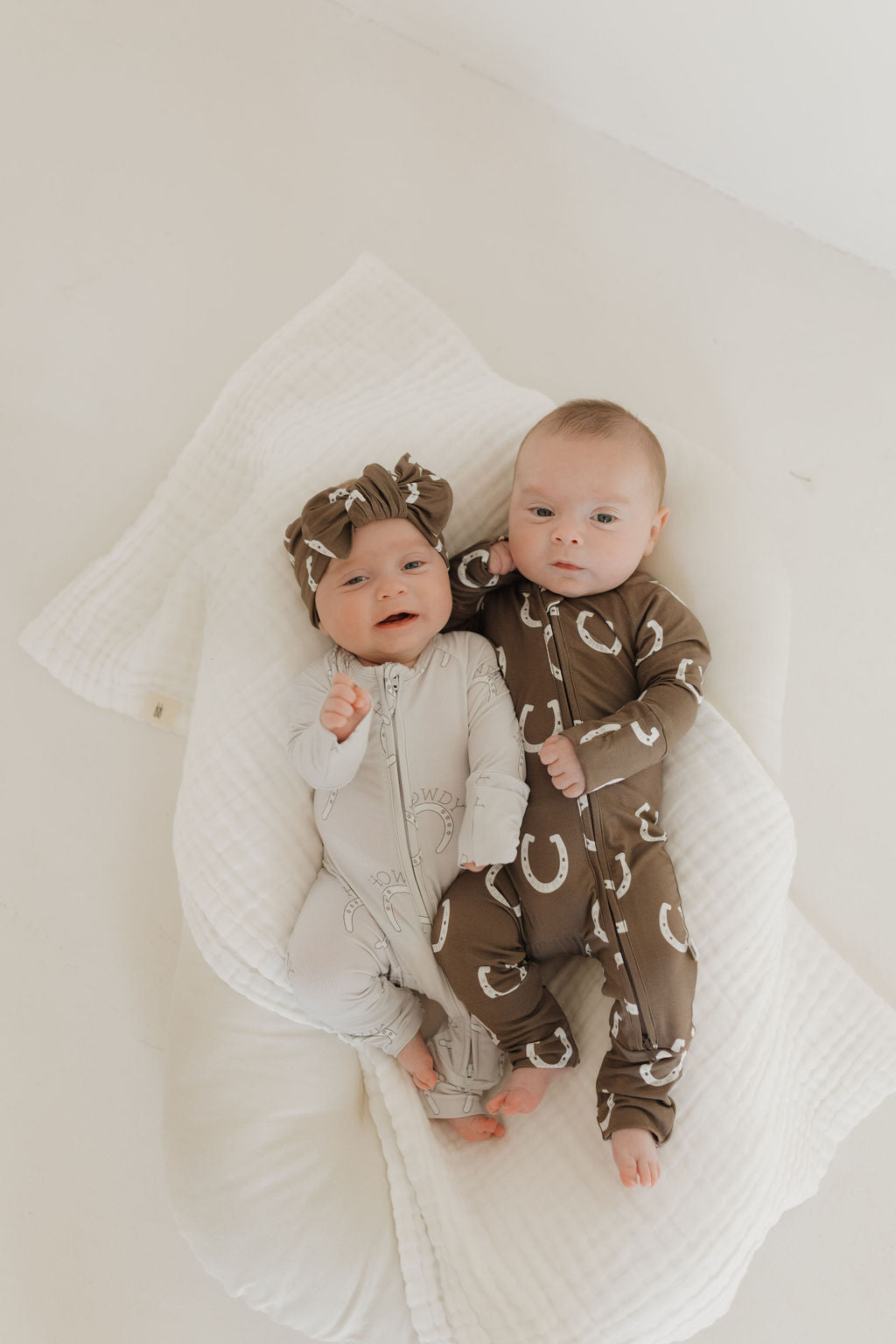 Two babies in bamboo zip pajamas with cowboy prints on a soft blanket, promoting a playful bedtime vibe.