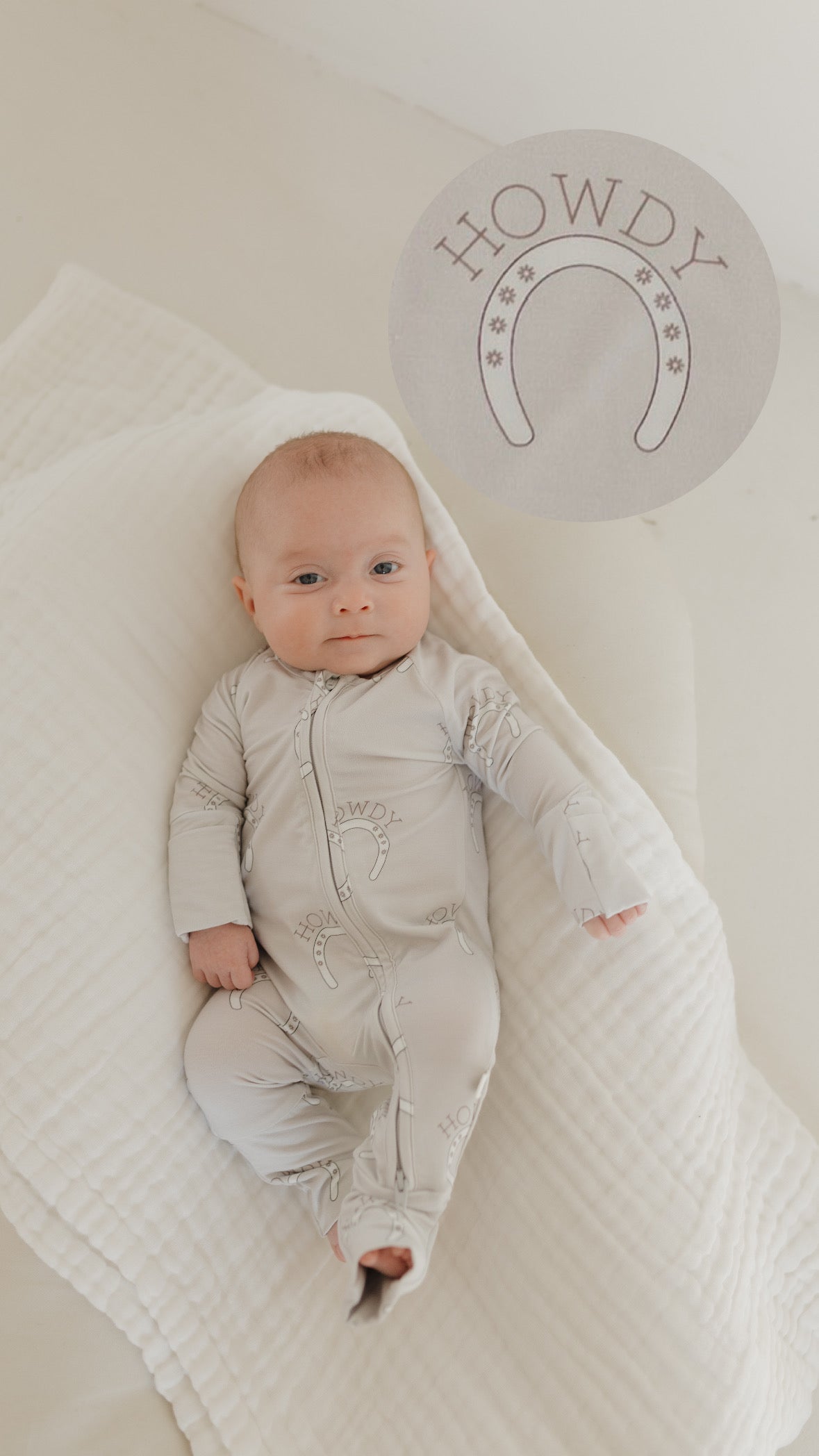 Baby wearing bamboo zip pajamas with 'Howdy' print, lying on a soft blanket.