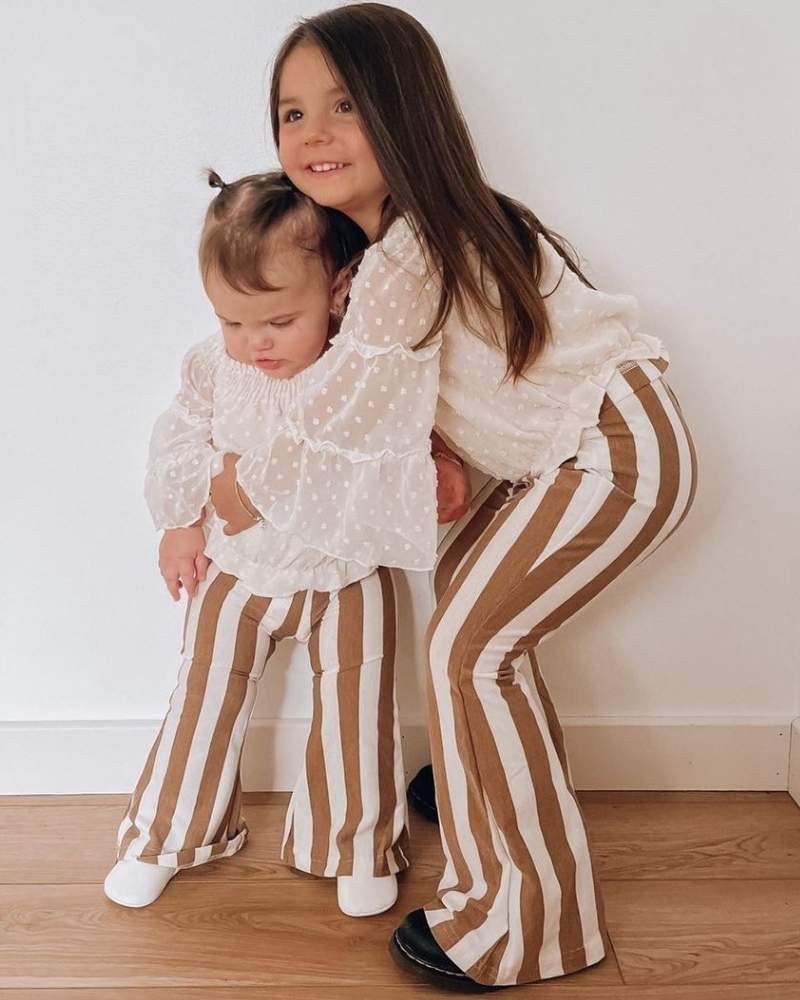 Two kids wearing tan striped bell bottom pants, showcasing playful vintage style and comfort.