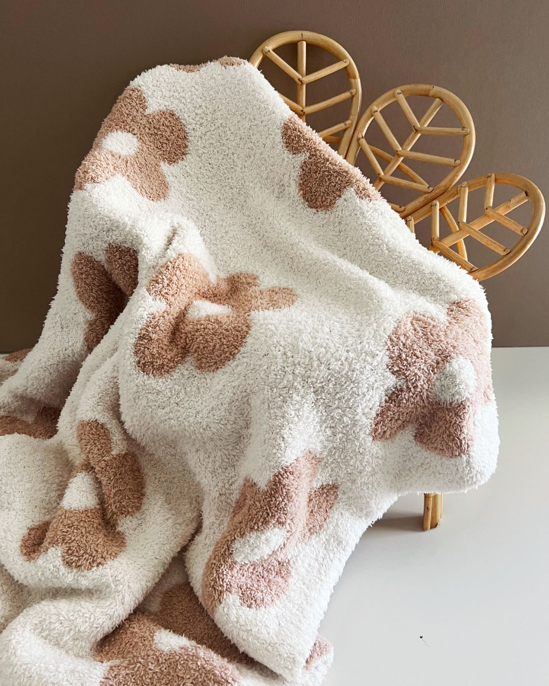 Daisy Fuzzy Blanket in latte with floral design, showcasing its plush texture on a modern chair.