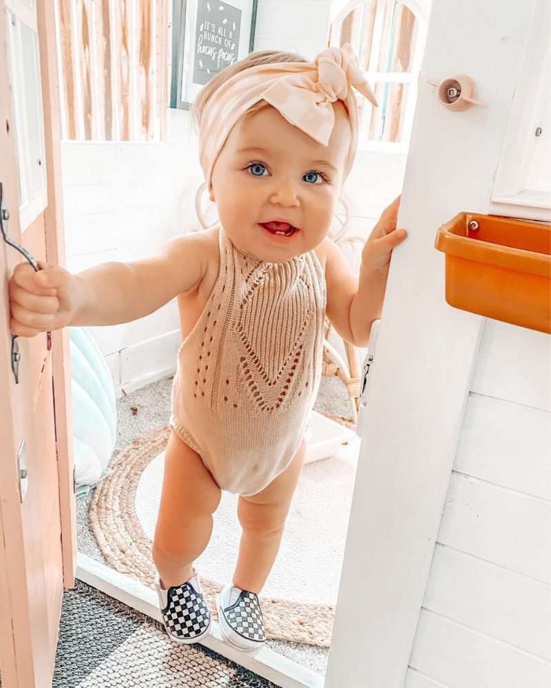 Adorable baby in Drake crochet halter romper, smiling at the door, showcasing soft vanilla cream fabric.