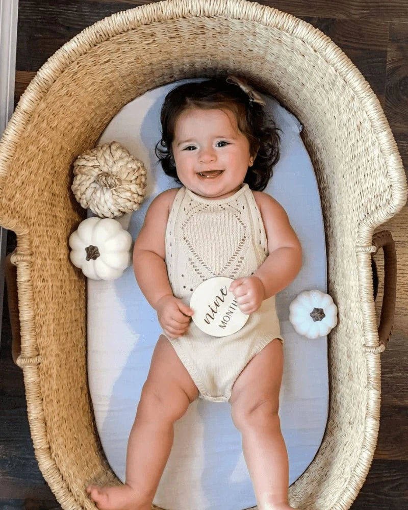 Adorable baby in crochet romper surrounded by decorative pumpkins in a cozy basket.