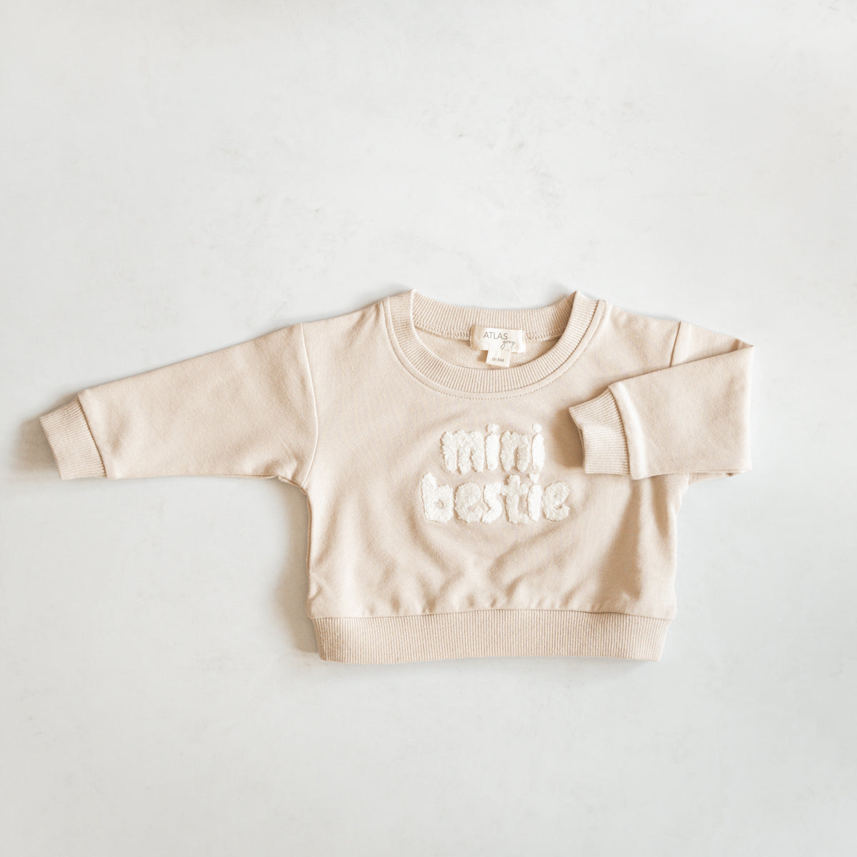 Mini Bestie Crewneck unisex baby sweatshirt in soft beige with fuzzy terry-cloth embroidery, ideal for cozy wear.