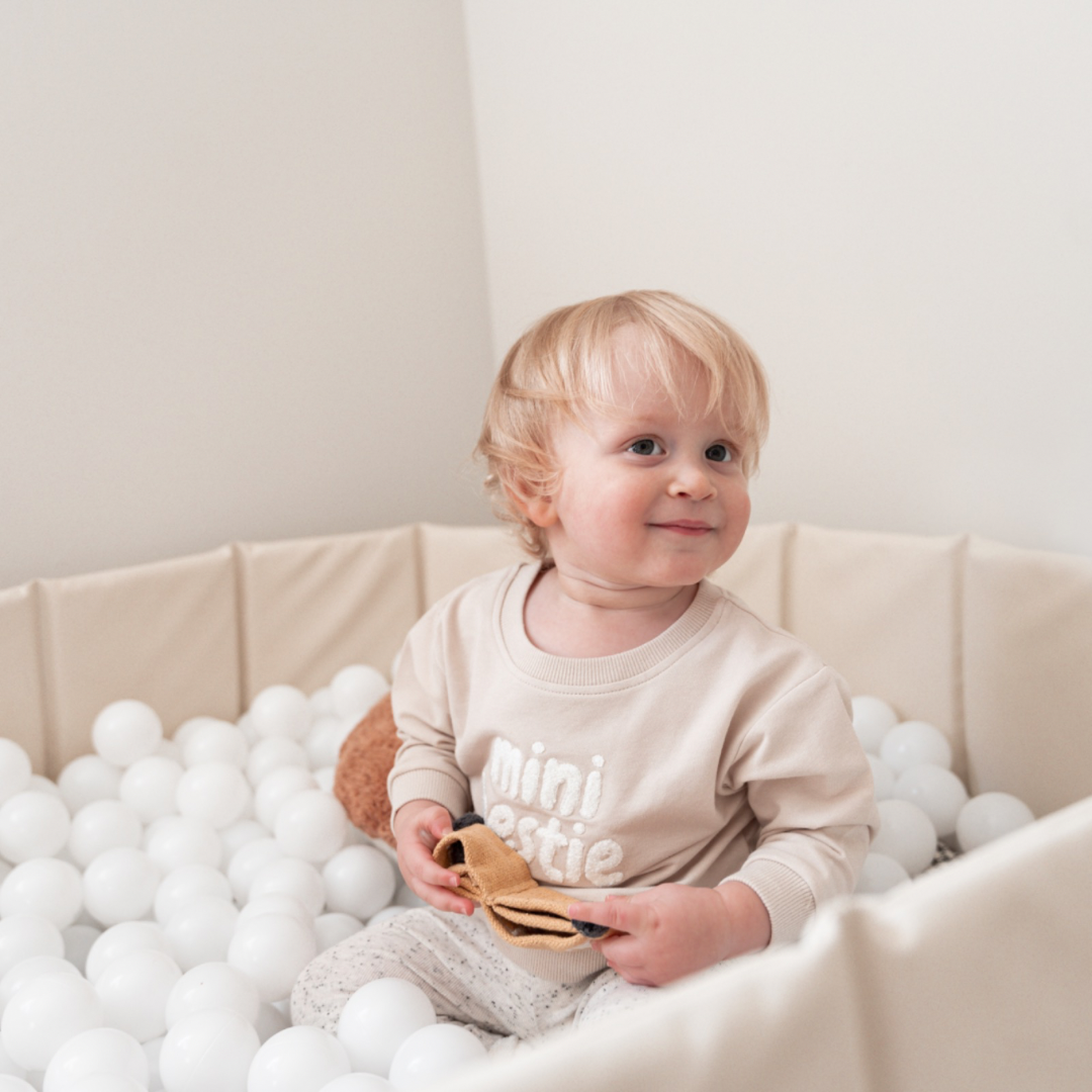 Baby wearing Mini Bestie Crewneck unisex sweatshirt sitting in a ball pit with a toy.
