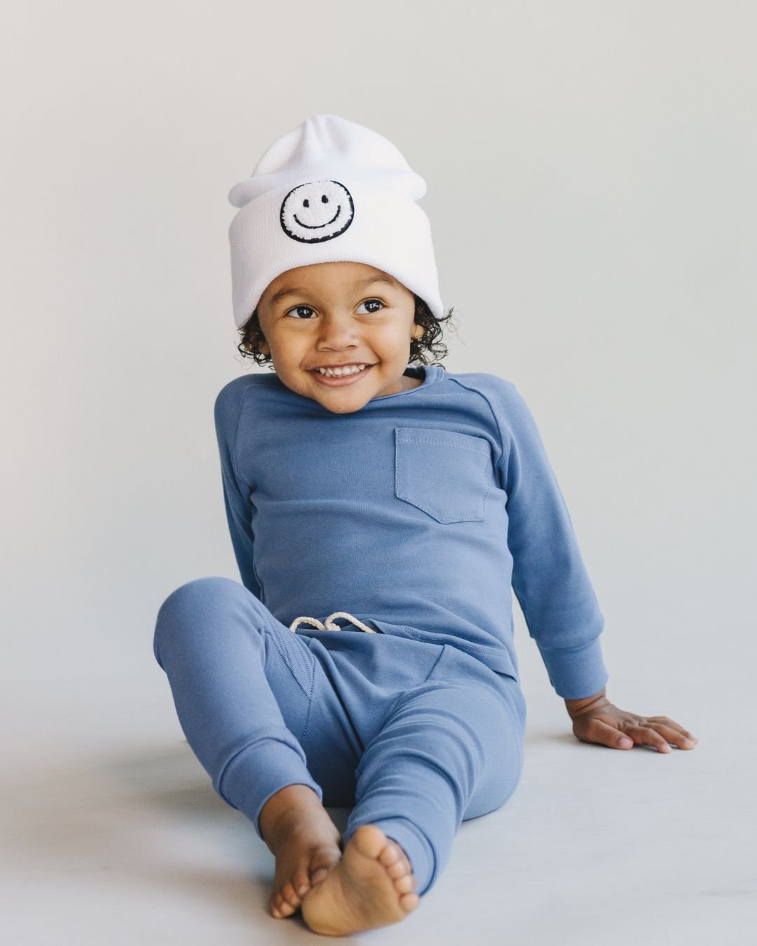 Smiley Beanie on a happy toddler wearing a blue outfit, showcasing comfort and style for cold weather.