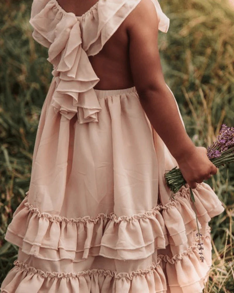 Back view of a girl in a champagne ruffle maxi dress, holding lavender flowers in a field.