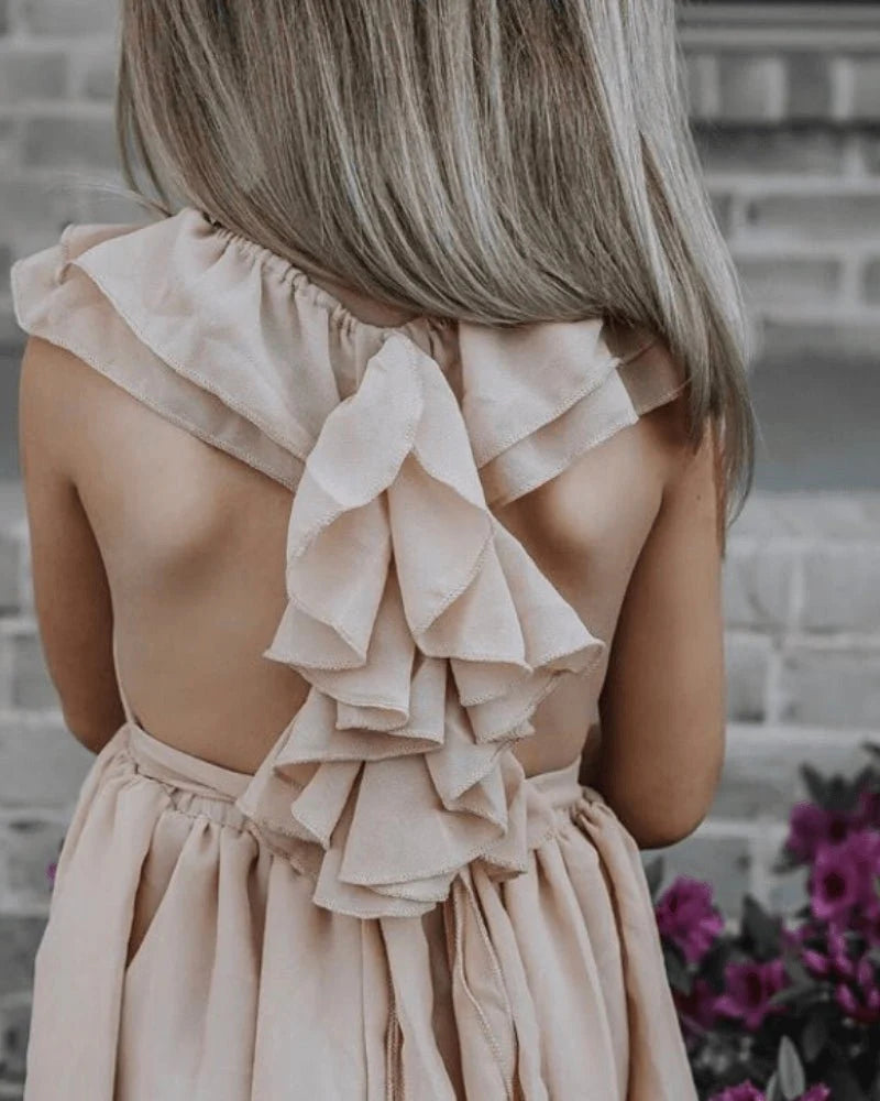 Back view of a girl wearing a champagne dress with ruffled details, showcasing delicate smocking and adjustable straps.
