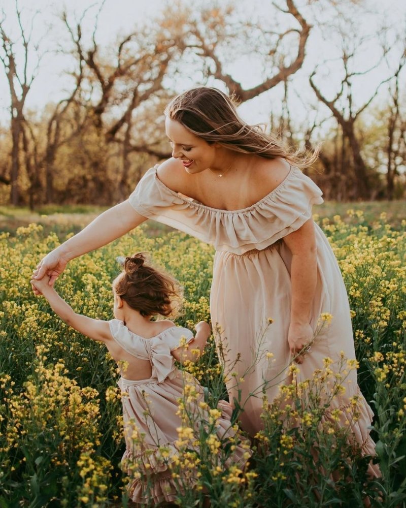 Mom and daughter in matching champagne dresses enjoying a sunny day in a flower field.