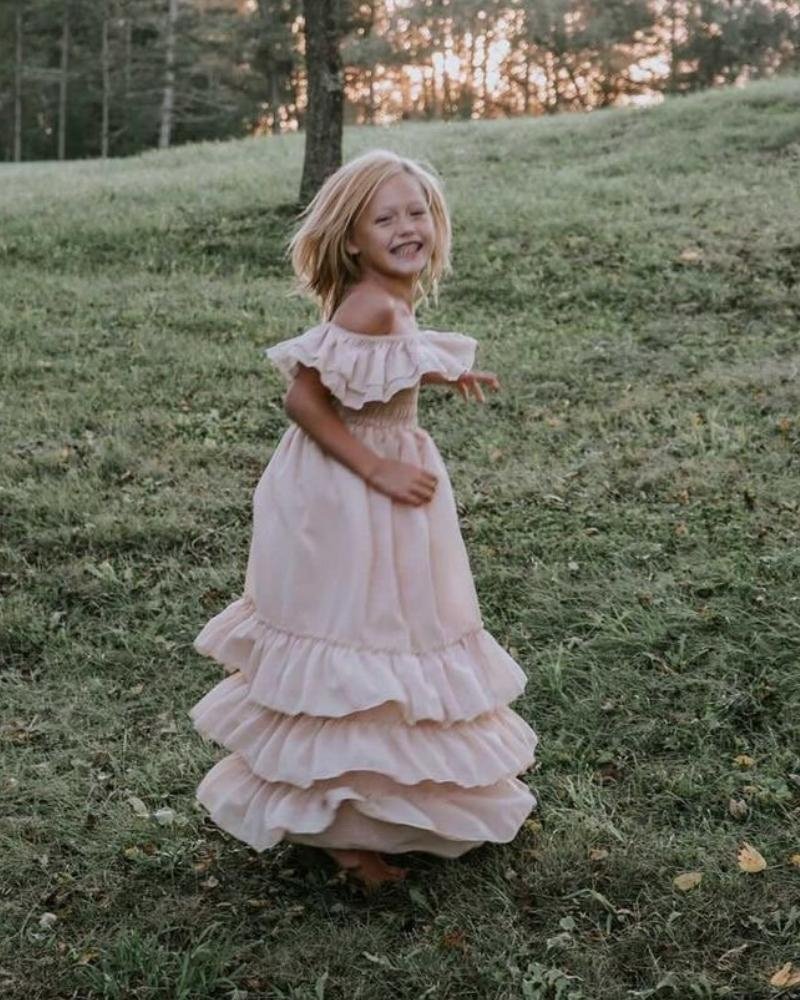 Girl twirling in a champagne ruffle maxi dress outdoors, showcasing playful elegance and light movement.