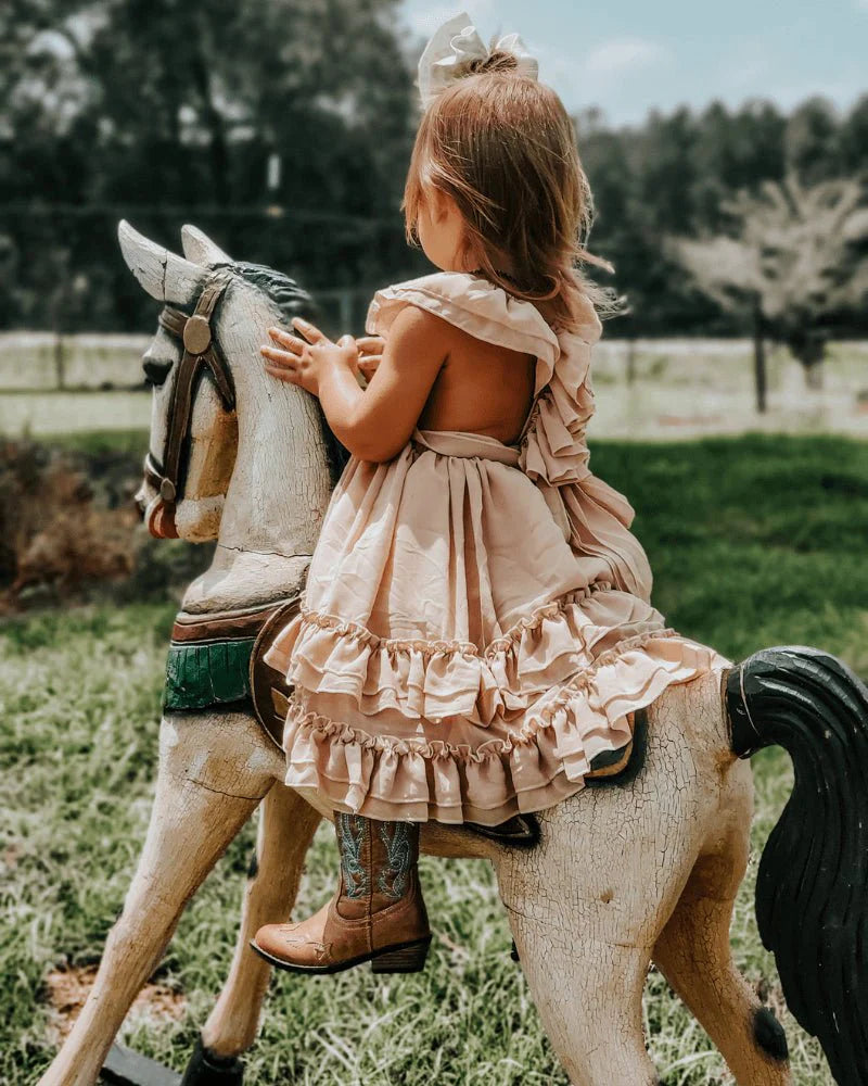 Girl in a champagne dress riding a toy horse, showcasing ruffles and playful style for special moments.