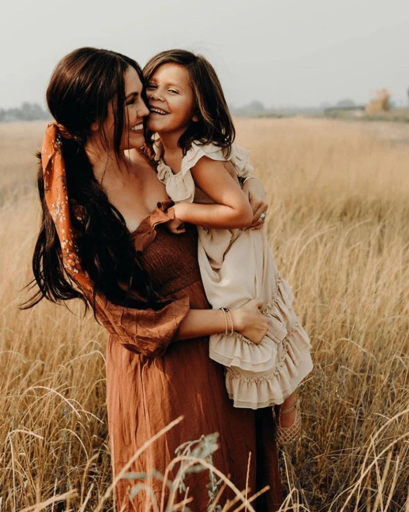 Mother and daughter joyfully embracing in a grassy field, capturing a warm, loving moment.