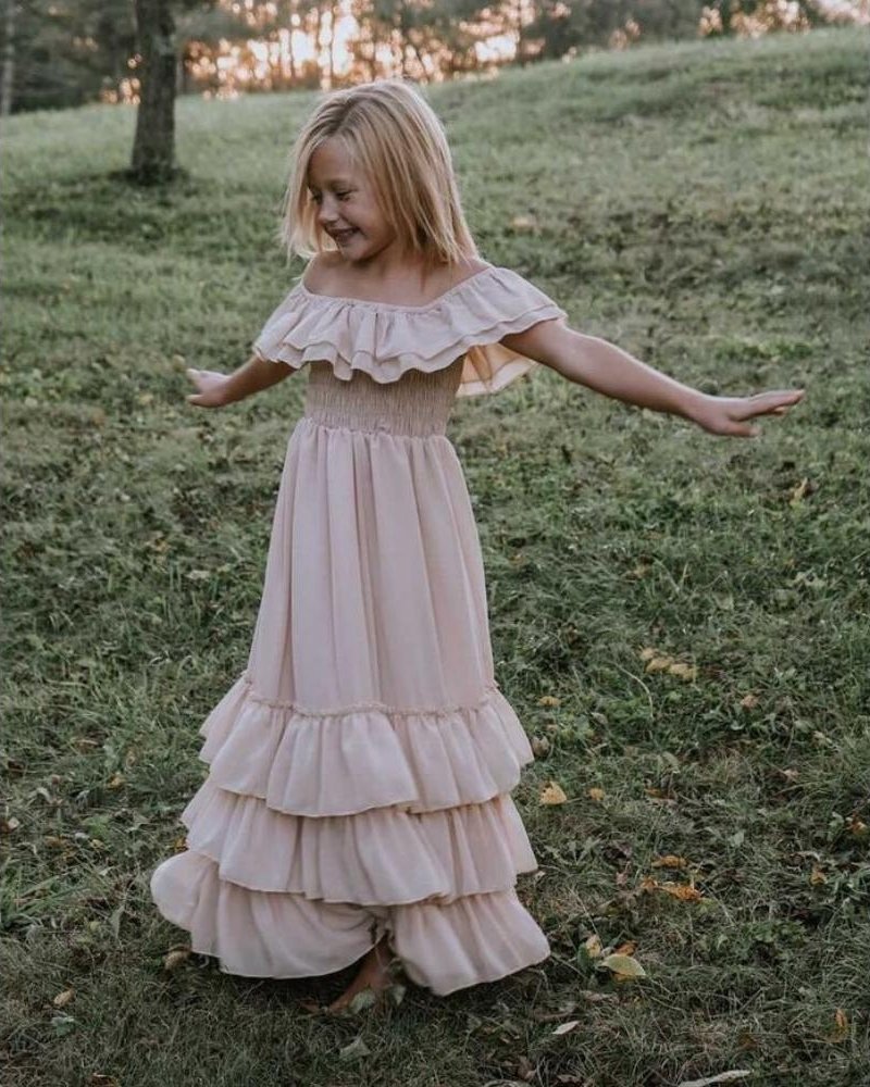 Girl twirling in a champagne dress with layered ruffles in a scenic outdoor setting.