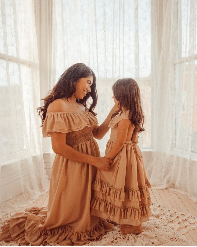 Mother and daughter wearing champagne dresses, showcasing the Nellie Ruffle Maxi Dress in a cozy, bright setting.