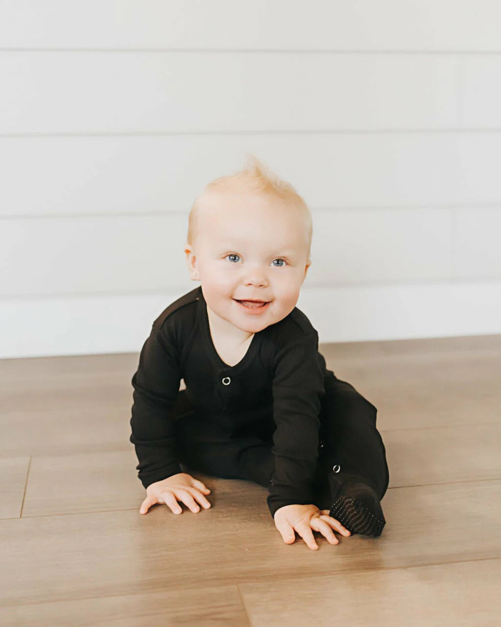 Smiling baby wearing a black organic snap footie, showcasing a soft and simple design, perfect for comfort and ease.
