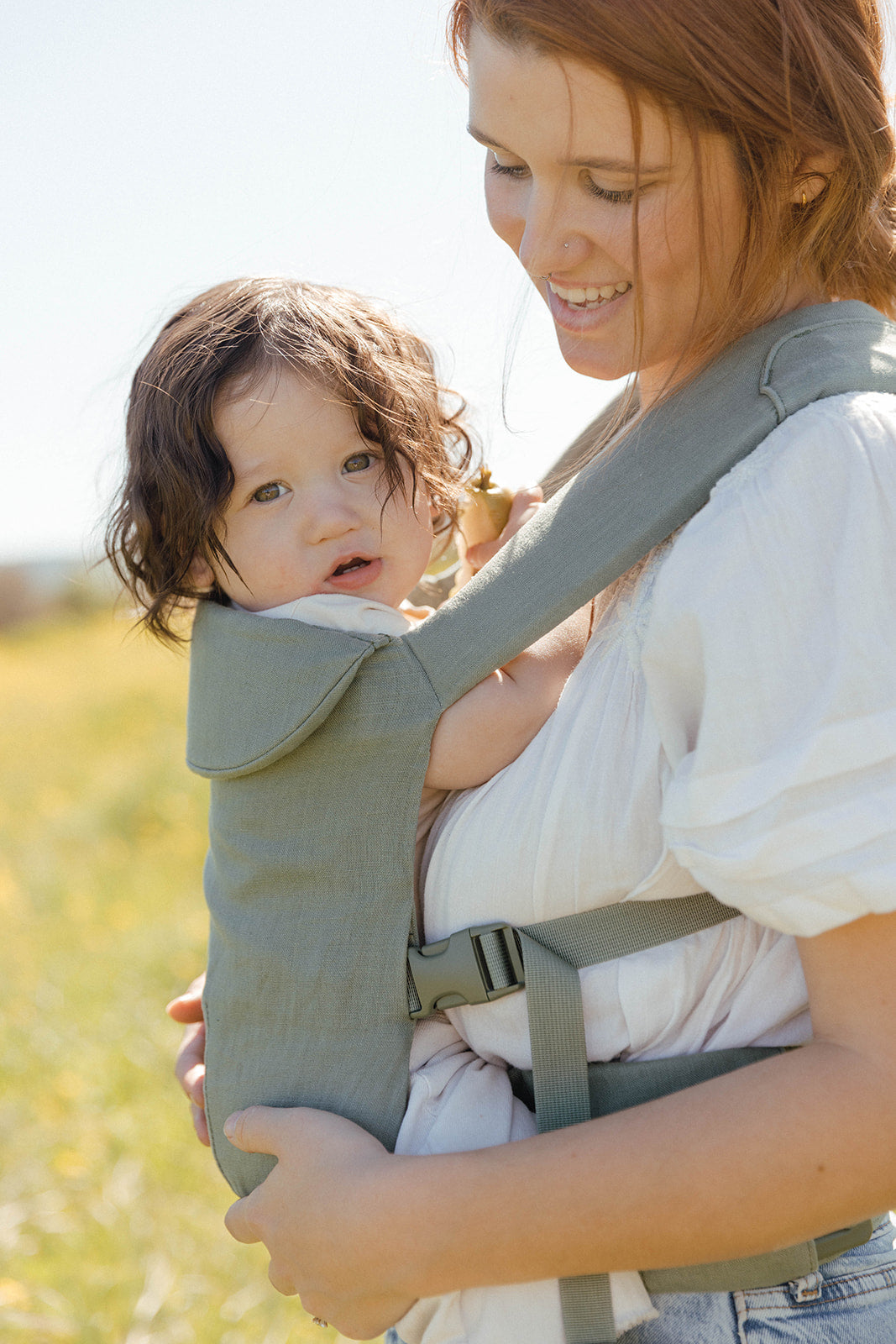 Acadian Aerial Carrier in dusky sage green, used by a mother with her baby outdoors, showcasing color-matched straps and buckles.